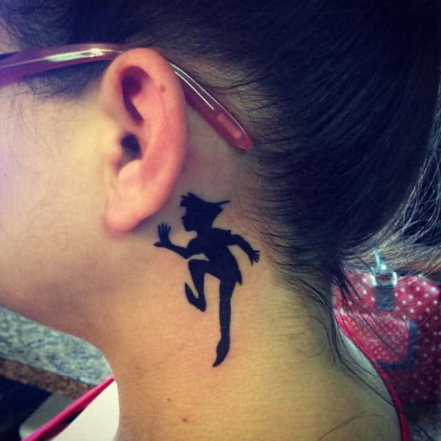 Black silhouette tattoo of Peter Pan in a playful pose behind the ear, symbolizing adventure and youthfulness