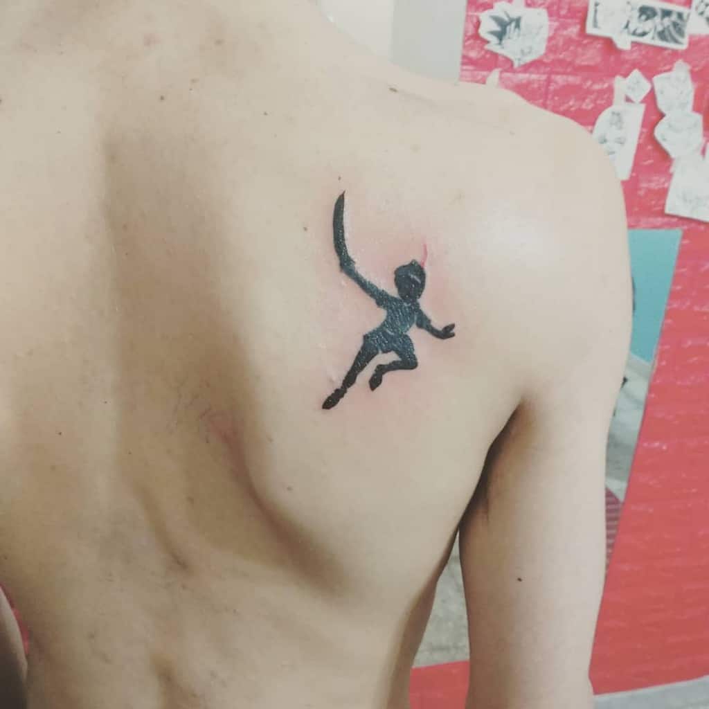 Black silhouette tattoo of Peter Pan swinging a sword, placed on the upper back, symbolizing adventure and courage