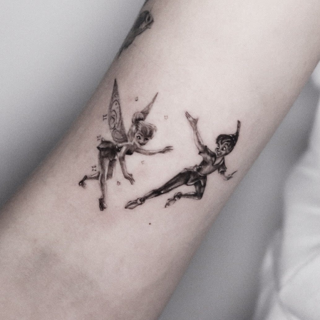 Delicate black and grey tattoo of Peter Pan and Tinker Bell flying together, surrounded by tiny sparkling stars
