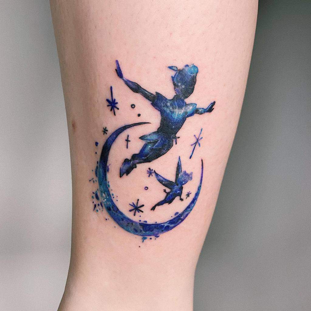 Vibrant blue tattoo of Peter Pan and Tinker Bell flying around a crescent moon, surrounded by sparkling stars, creating a dreamy night-sky effect
