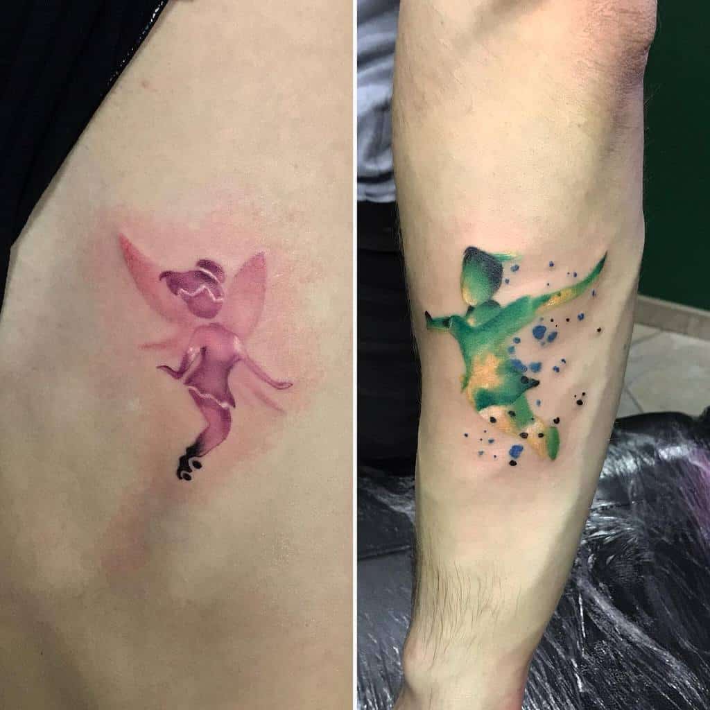 Matching watercolor tattoos of Tinker Bell in soft pink tones and Peter Pan in vibrant green with blue splashes, creating a dreamy, artistic effect