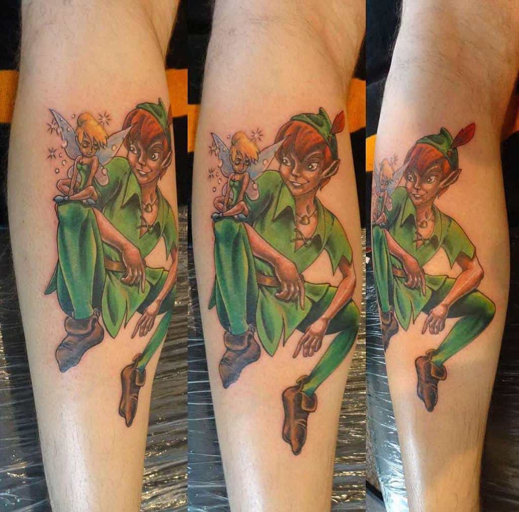 Vibrant tattoo of Peter Pan crouching with a playful grin, holding Tinker Bell in his hand as she sprinkles pixie dust, detailed with rich colors
