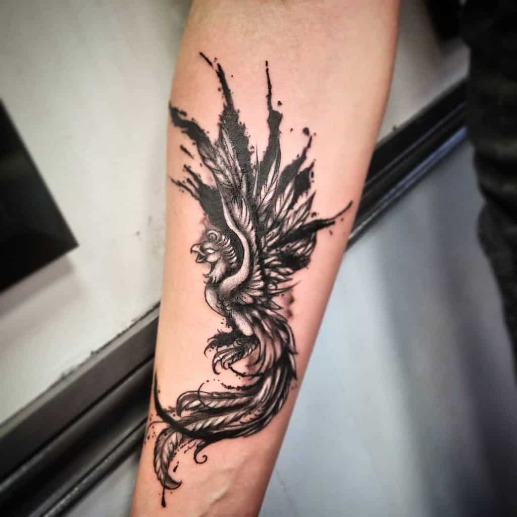 Forearm tattoo of a phoenix rising with detailed black and grey ink work and splashes of abstract design