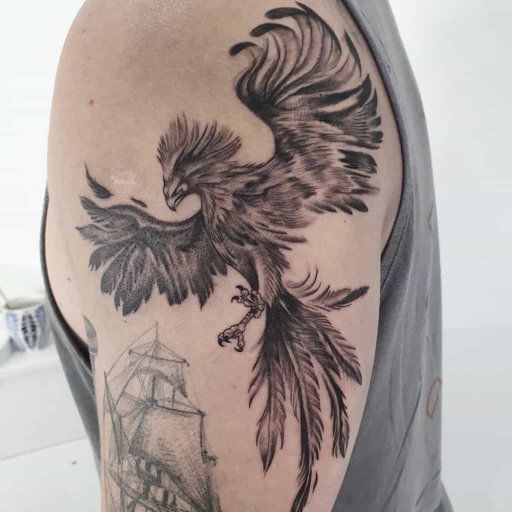 Tattoo of a phoenix rising with spread wings and detailed feathers on a person's upper arm