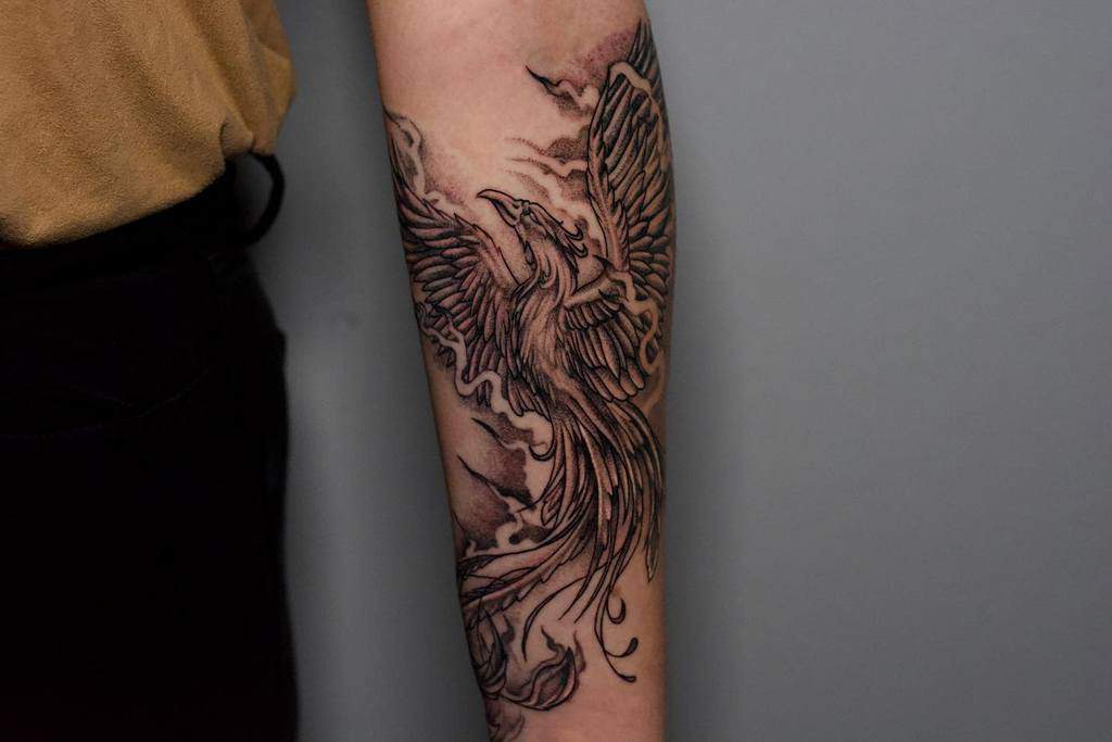 A detailed phoenix rising tattoo on a person's forearm, surrounded by fire and smoke