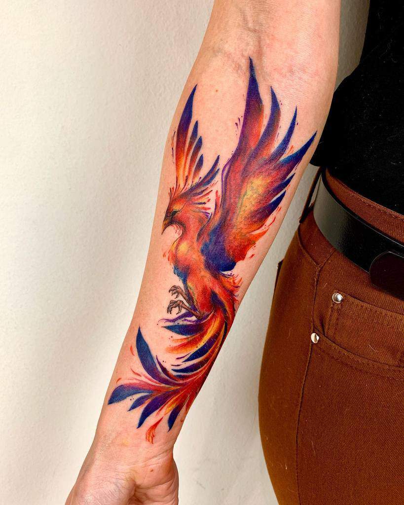 Colorful phoenix tattoo on a forearm with vibrant red, orange, and blue hues