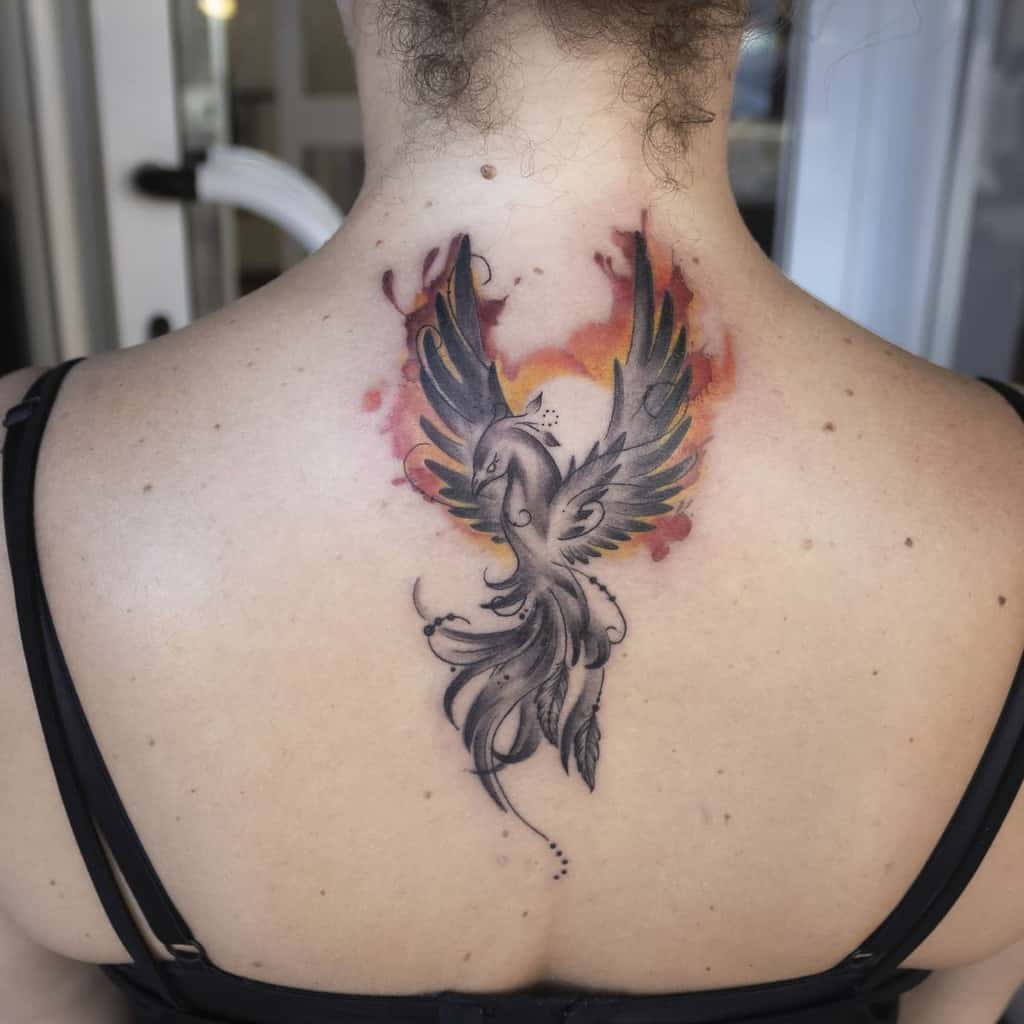 Back tattoo of a phoenix rising in black and red ink, centered between the shoulders