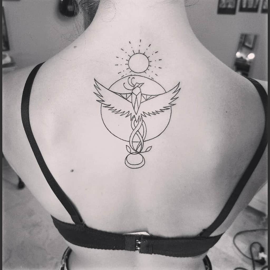 Black and white tattoo of a phoenix rising with sun and geometric shapes on a person's upper back