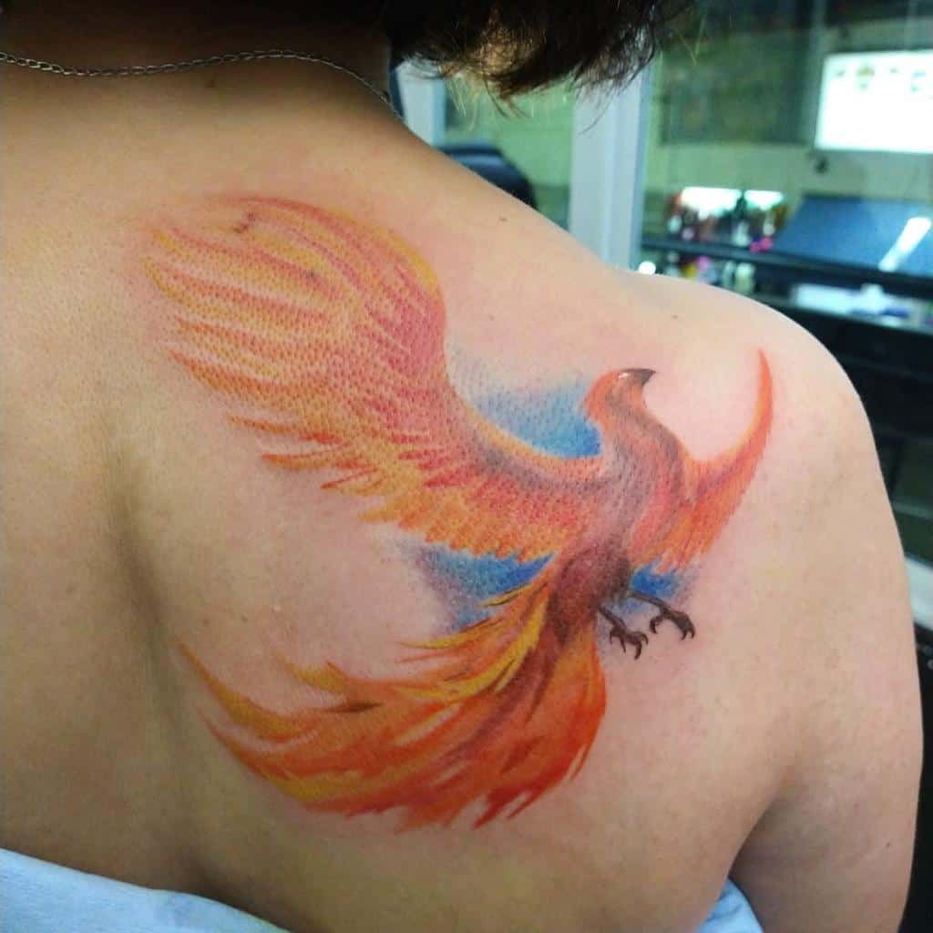A colorful phoenix rising tattoo is displayed on a person's shoulder