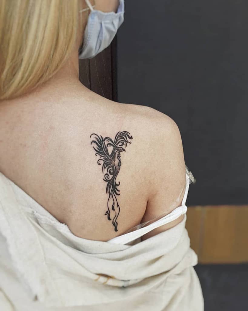Woman with a black phoenix rising tattoo on her upper back