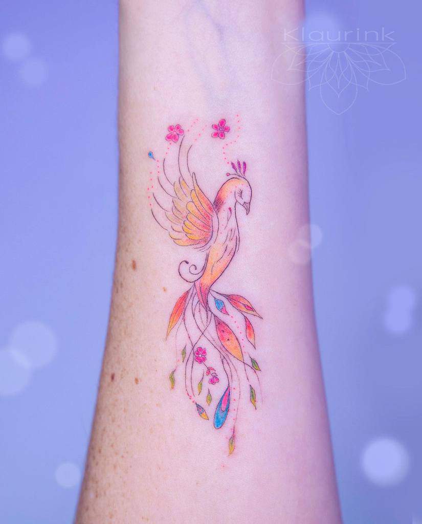 Colorful tattoo of a phoenix rising with flowers on a person's forearm