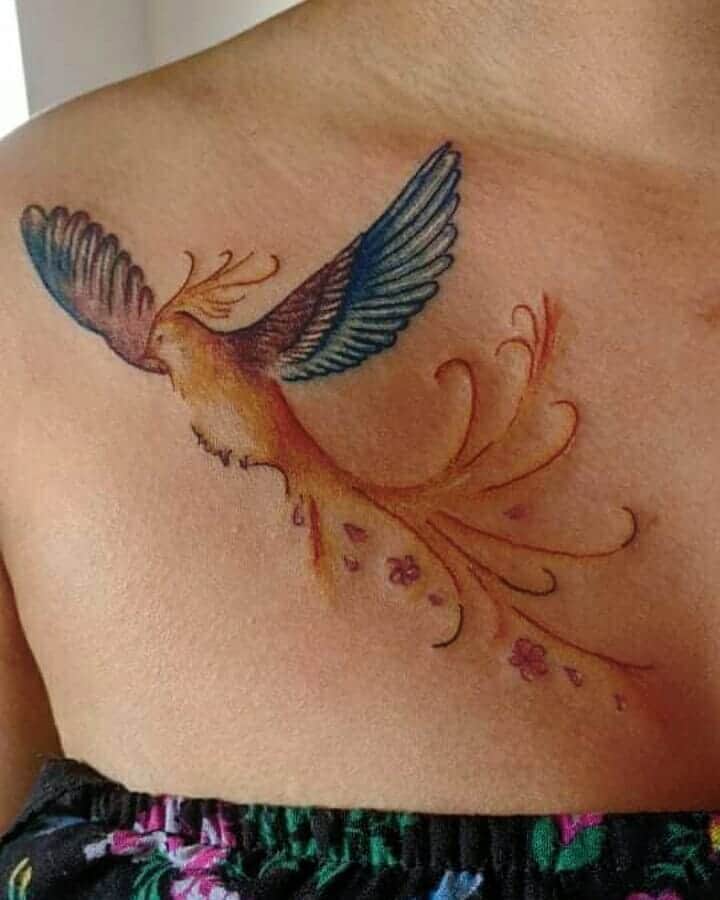 Colorful phoenix rising tattoo on a person's collarbone with flower details and ornate tail feathers
