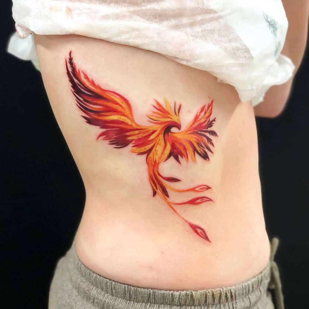 A vibrant phoenix rising tattoo with fiery hues on a side torso