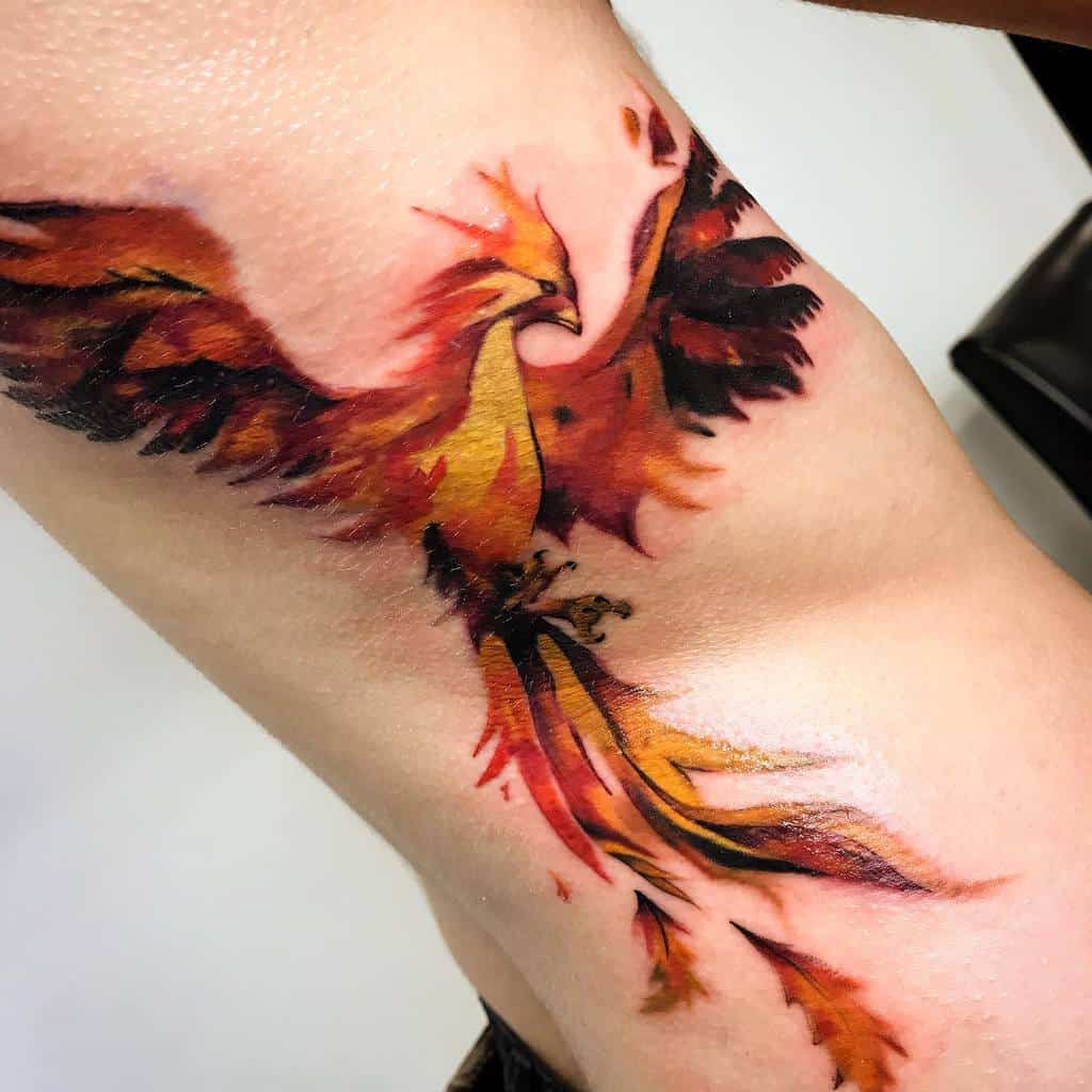 Vibrant phoenix rising tattoo with bold red, orange, and yellow hues on a person's inner forearm