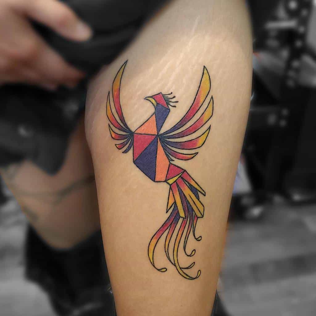 Geometric phoenix rising tattoo in red, orange, and purple on a person's thigh