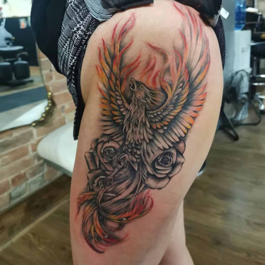 Tattoo of a phoenix rising from the ashes, beautifully intertwined with roses on a person's thigh