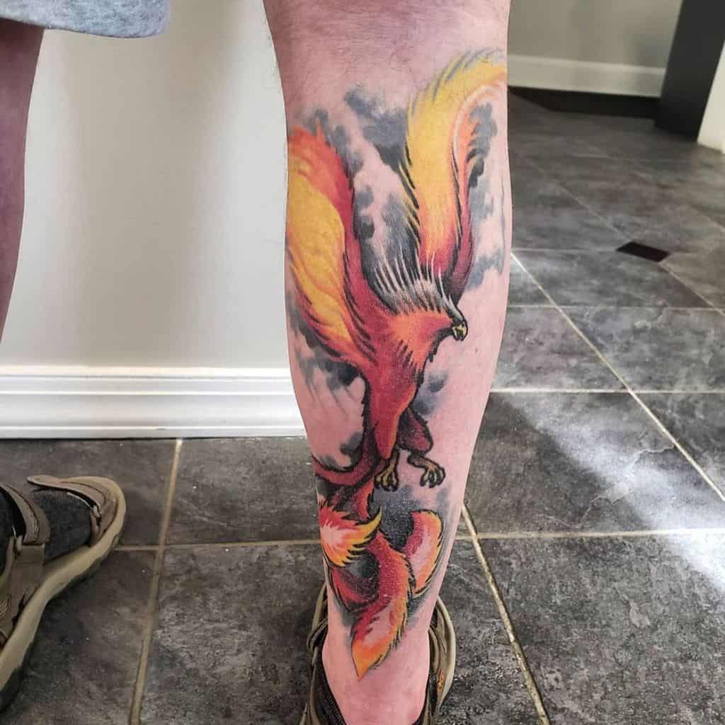 Leg tattoo featuring a vibrant phoenix rising in red, orange, and yellow hues with detailed wings and flames