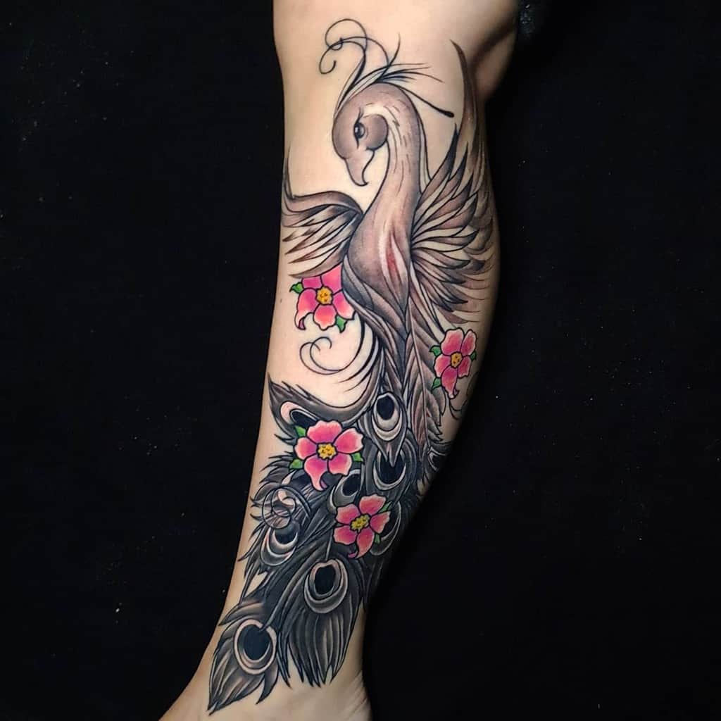 Leg tattoo of a stylized phoenix rising with floral elements and intricate black and grey shading