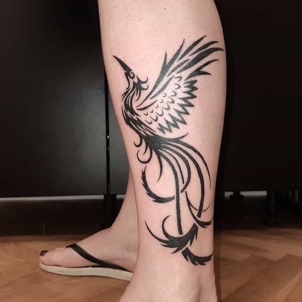 A stunning black phoenix rising tattoo graces a calf