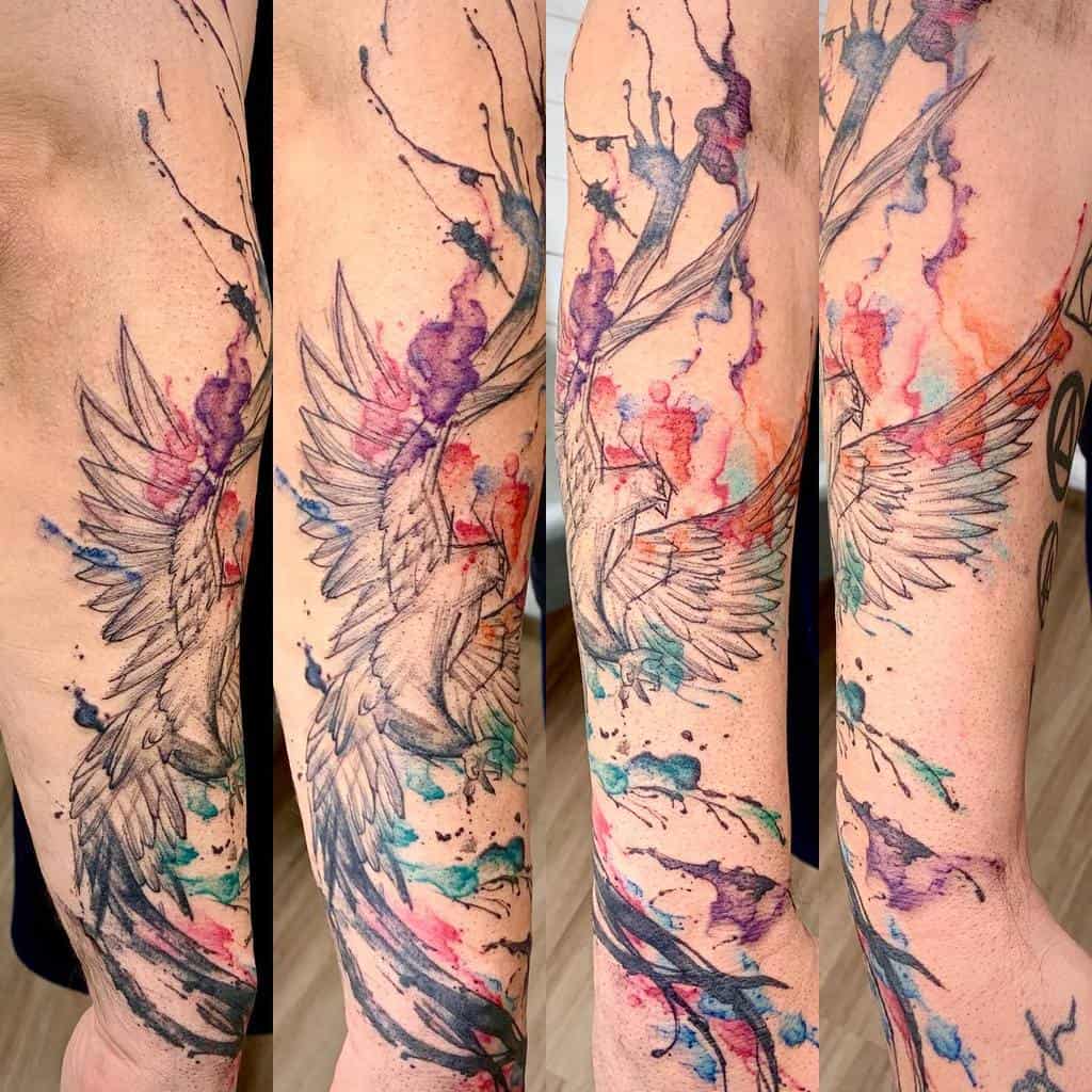 A forearm tattoo depicting a rising phoenix with colorful, watercolor-like splashes