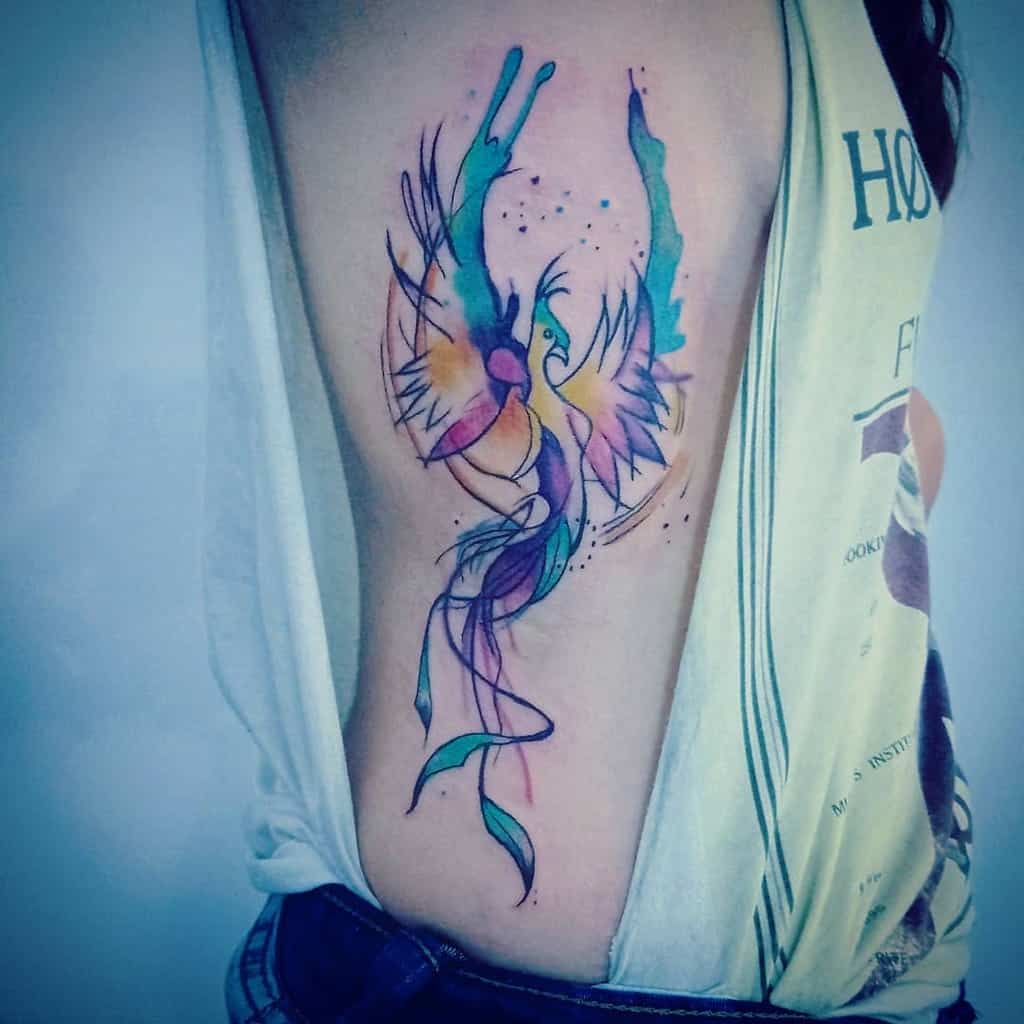 Watercolor-style tattoo of a colorful phoenix on a side torso