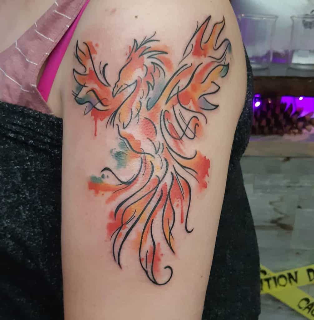 Tattoo of a colorful phoenix in a watercolor style on a person's upper arm