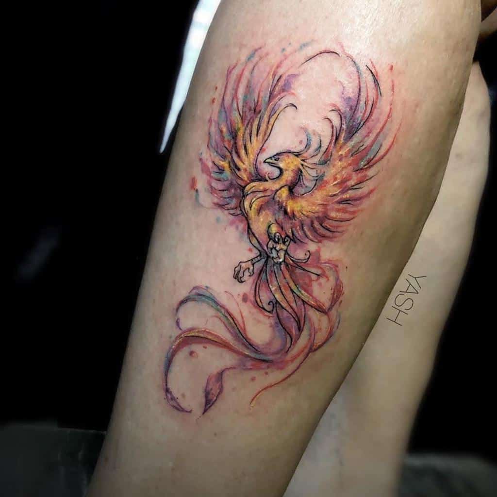Colorful watercolor-style phoenix tattoo on a person's forearm, featuring vibrant hues and light strokes