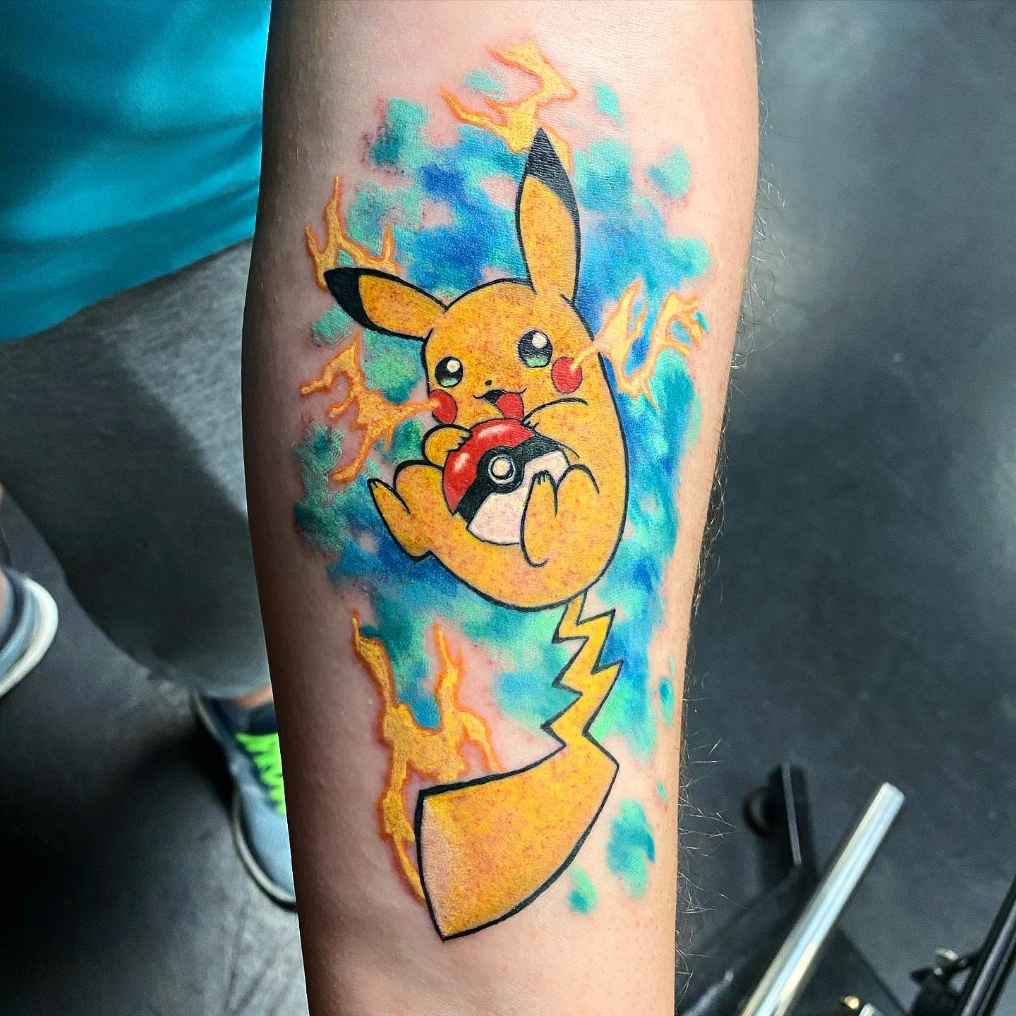 Vibrant tattoo of Pikachu holding a Poké Ball with lightning and flames on an arm