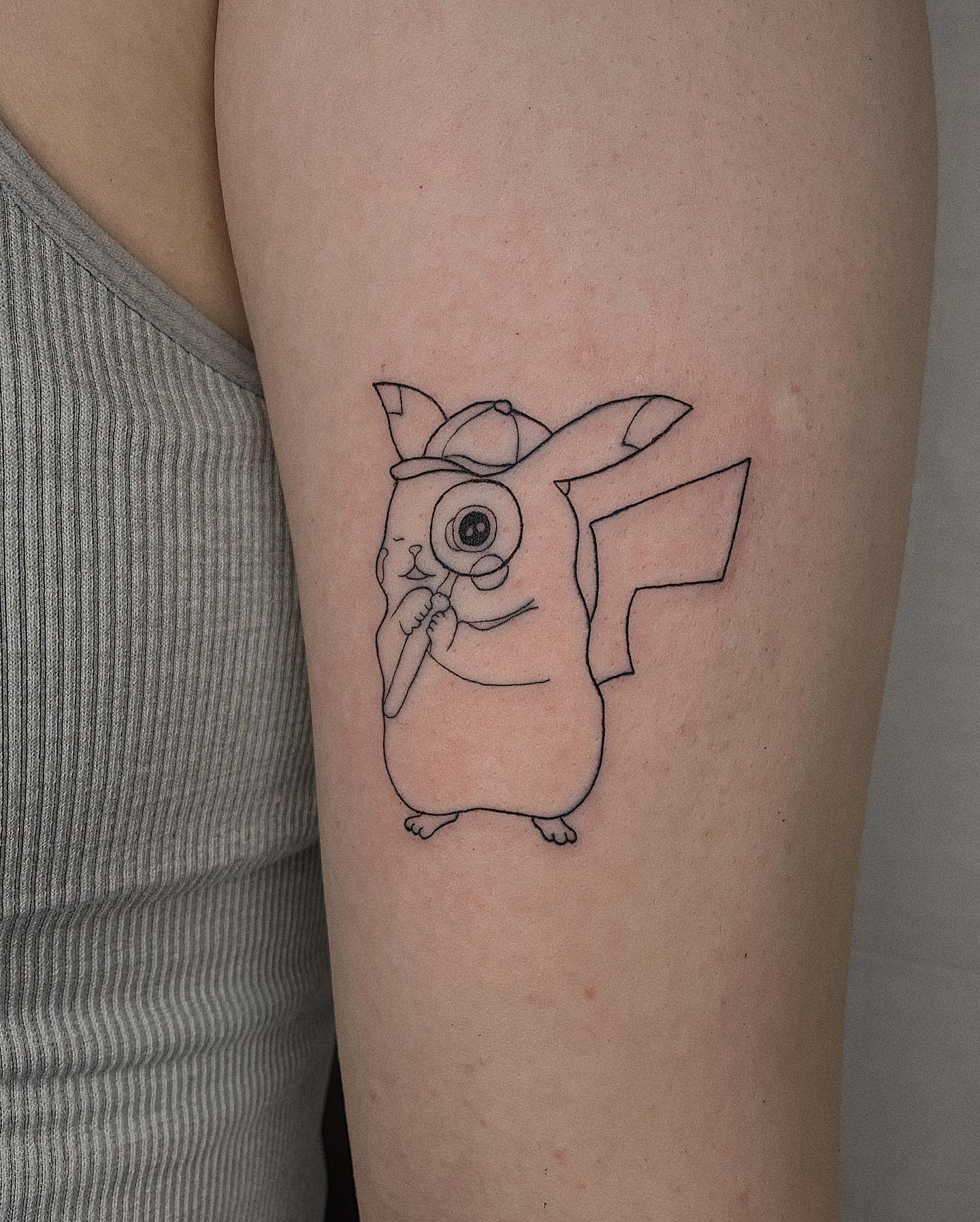 Tattoo of Pikachu in geometric style on upper arm, wearing a detective hat and holding a magnifying glass