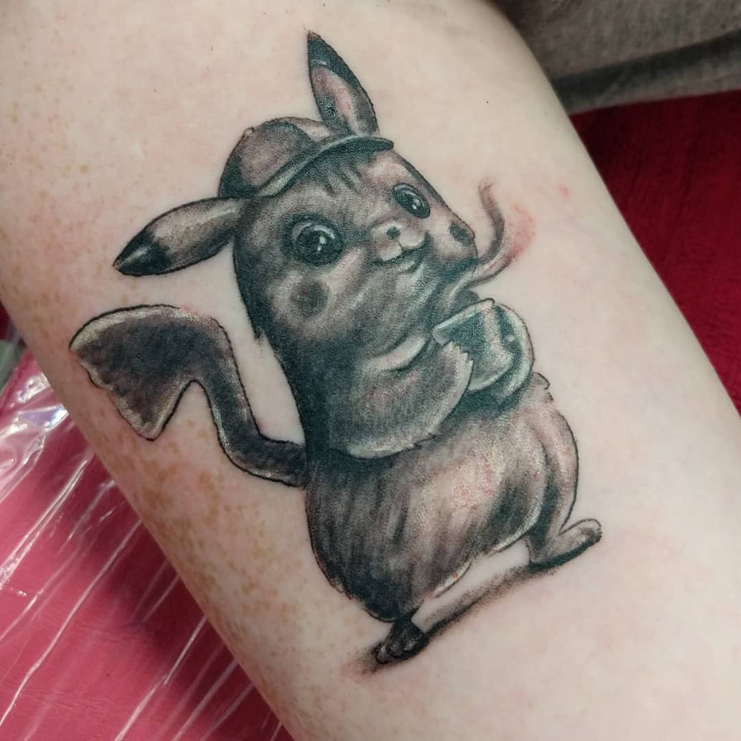 Tattoo of Pikachu dressed as a detective holding a magnifying glass and wearing a hat