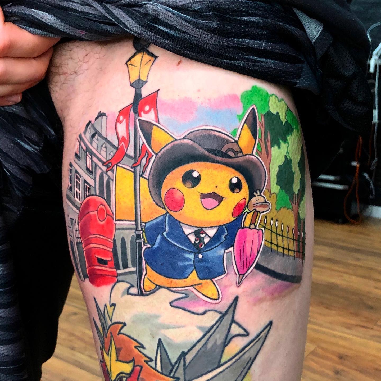 Colorful tattoo of Pikachu in a suit holding an umbrella with a city backdrop