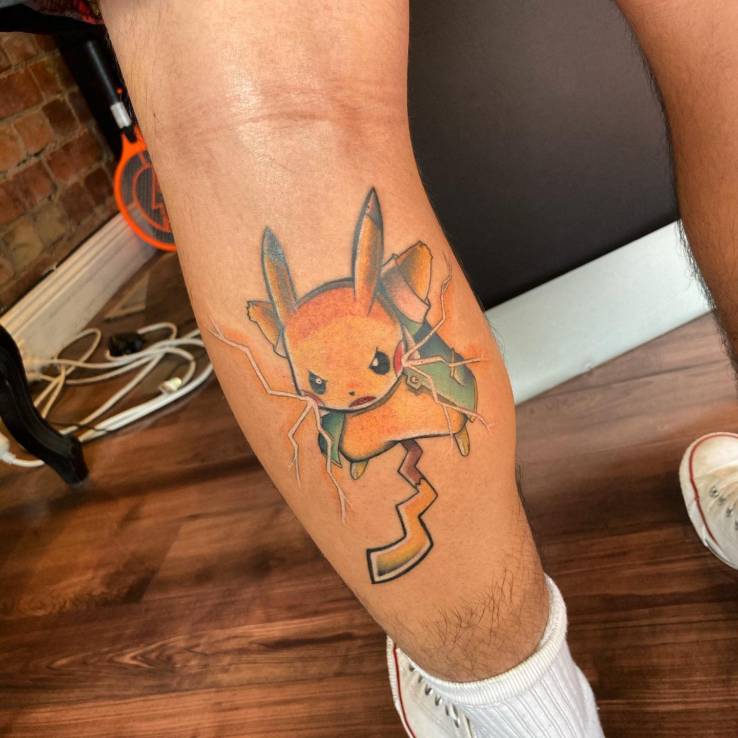 Tattoo of Pikachu breaking through skin on back of calf