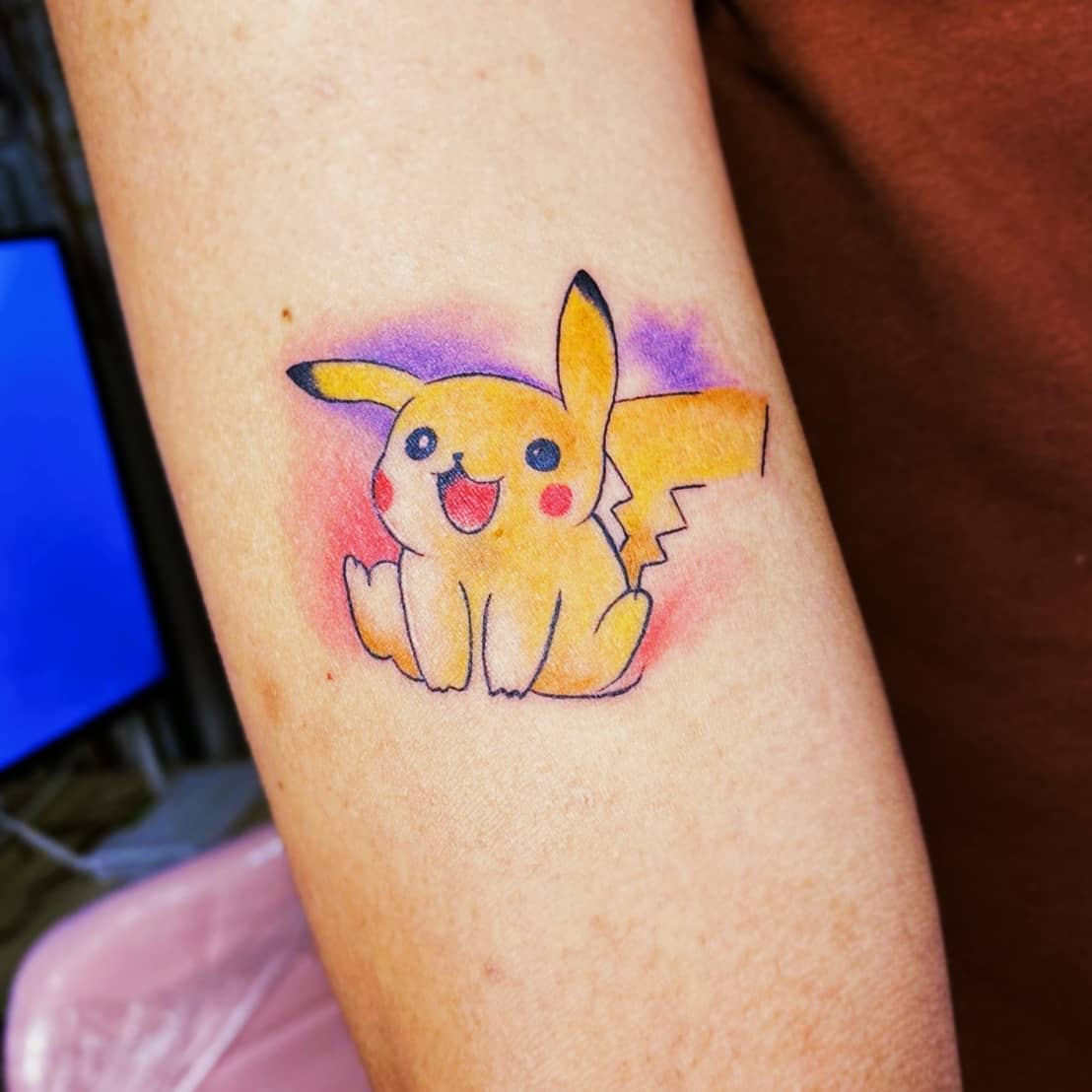 Tattoo of a smiling Pikachu on an arm with a colorful background