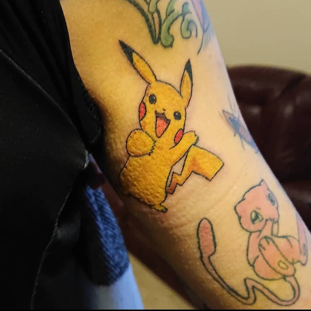 Tattoo of Pikachu and Mew on an arm with other colorful designs