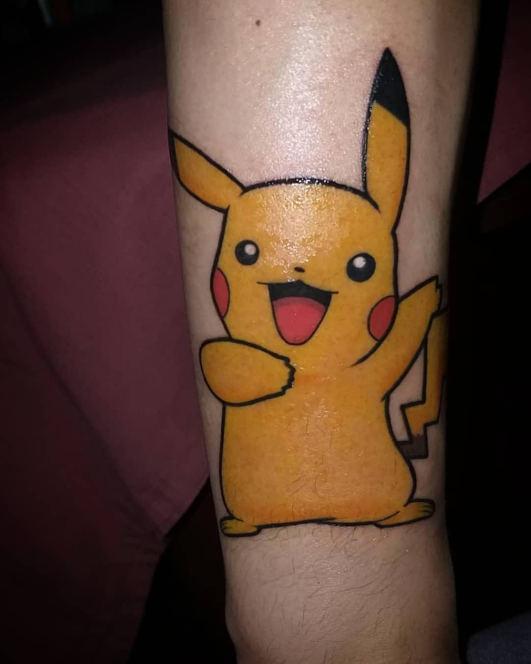 A tattoo on an arm of Pikachu, a yellow animated character, smiling and waving
