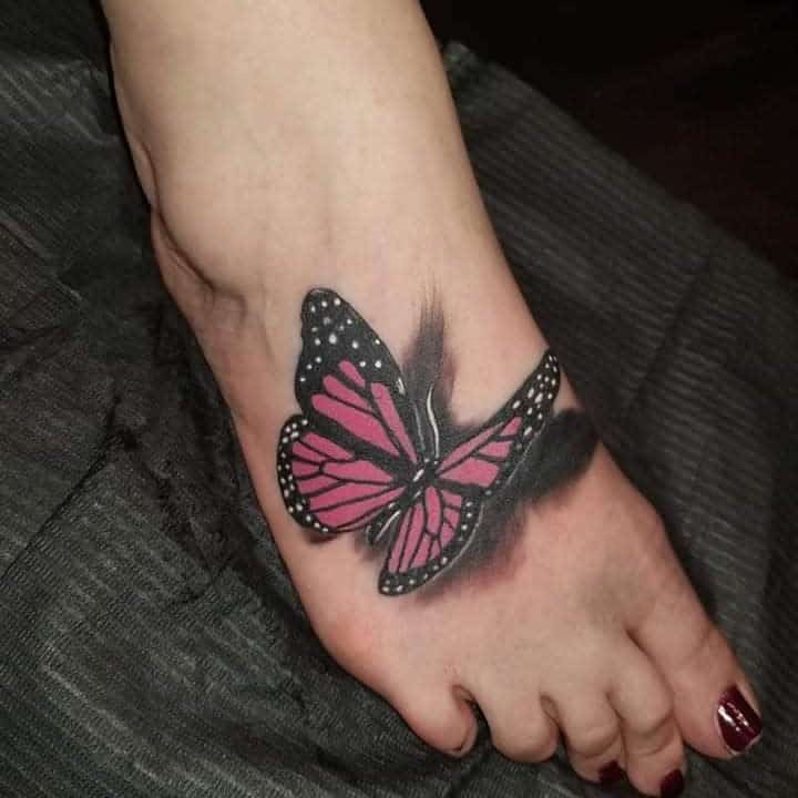 A pink and black butterfly tattoo on the top of a foot