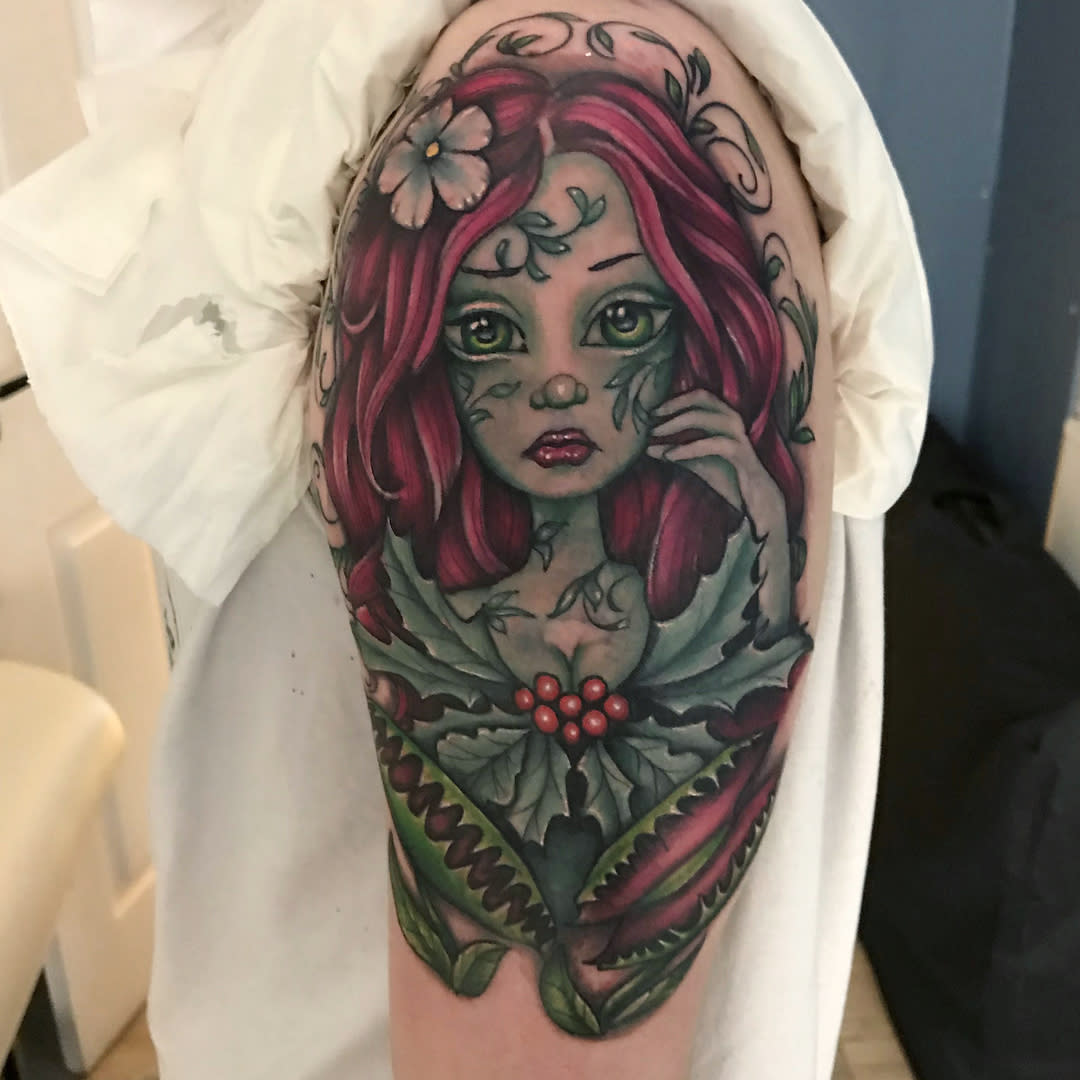 Tattoo of a fairy with pink hair, surrounded by leaves and berries on an upper arm