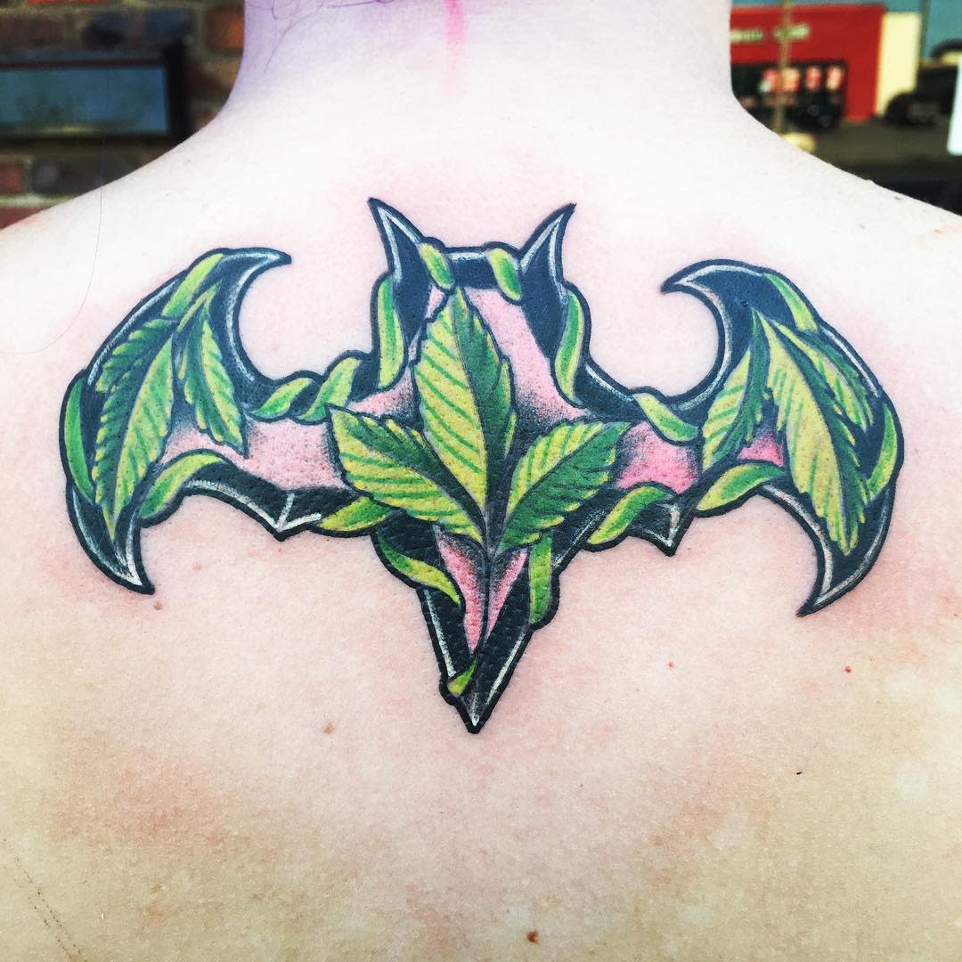 Tattoo of a bat shape filled with green poison ivy leaves on upper back