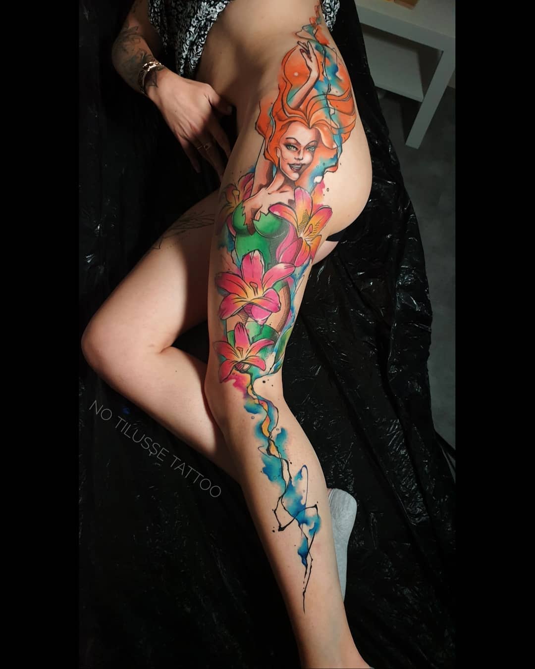 Colorful tattoo of a woman and flowers extending from hip to calf on a leg