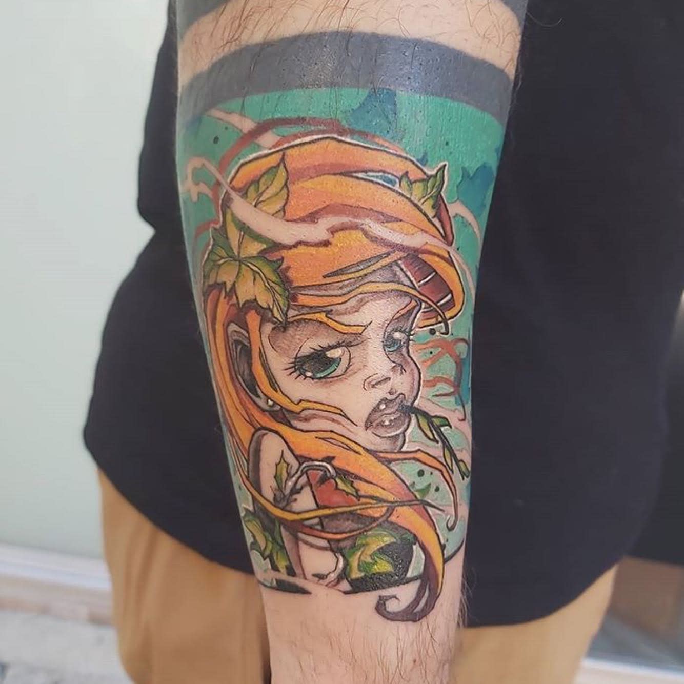 Colorful tattoo of a woman with orange hair and leaves on a forearm