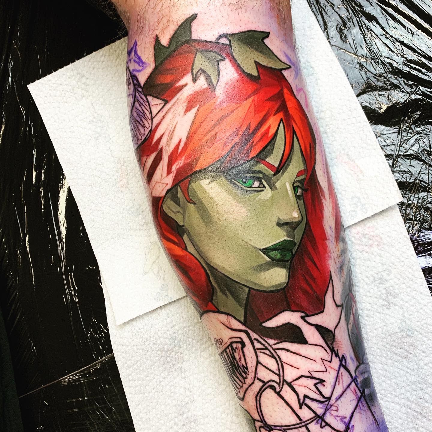 Tattoo of a green-skinned woman with red hair and leaves on her head on a leg