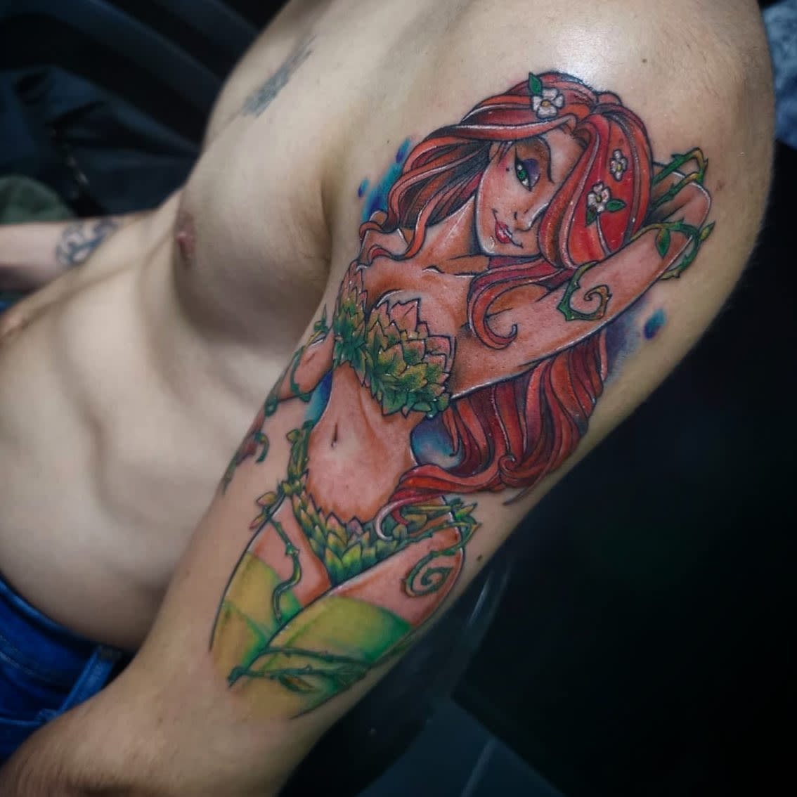 Colorful tattoo of a red-haired woman with poison ivy leaves on her body on an upper arm