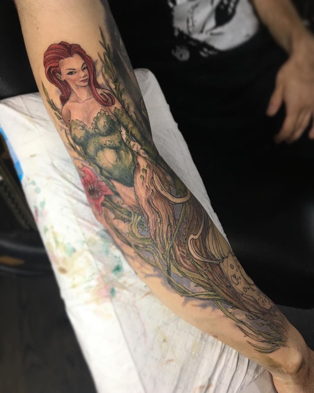 Tattoo of a woman with red hair and green attire blending with tree-like elements