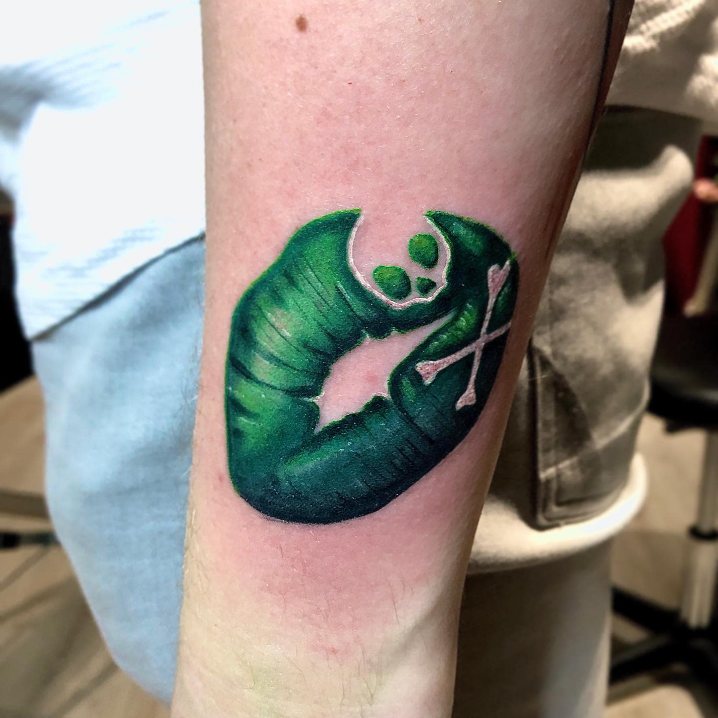 Tattoo of a green lip-like shape with a skull and crossbones inside on an arm