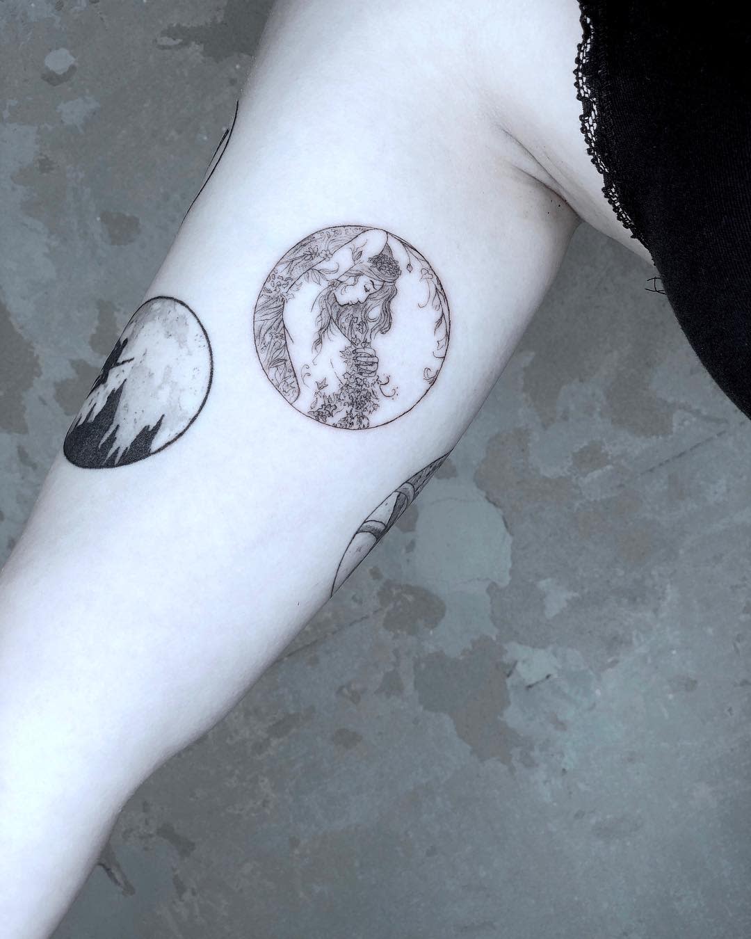 Two intricate black ink tattoos on an upper arm, one circular and one crescent