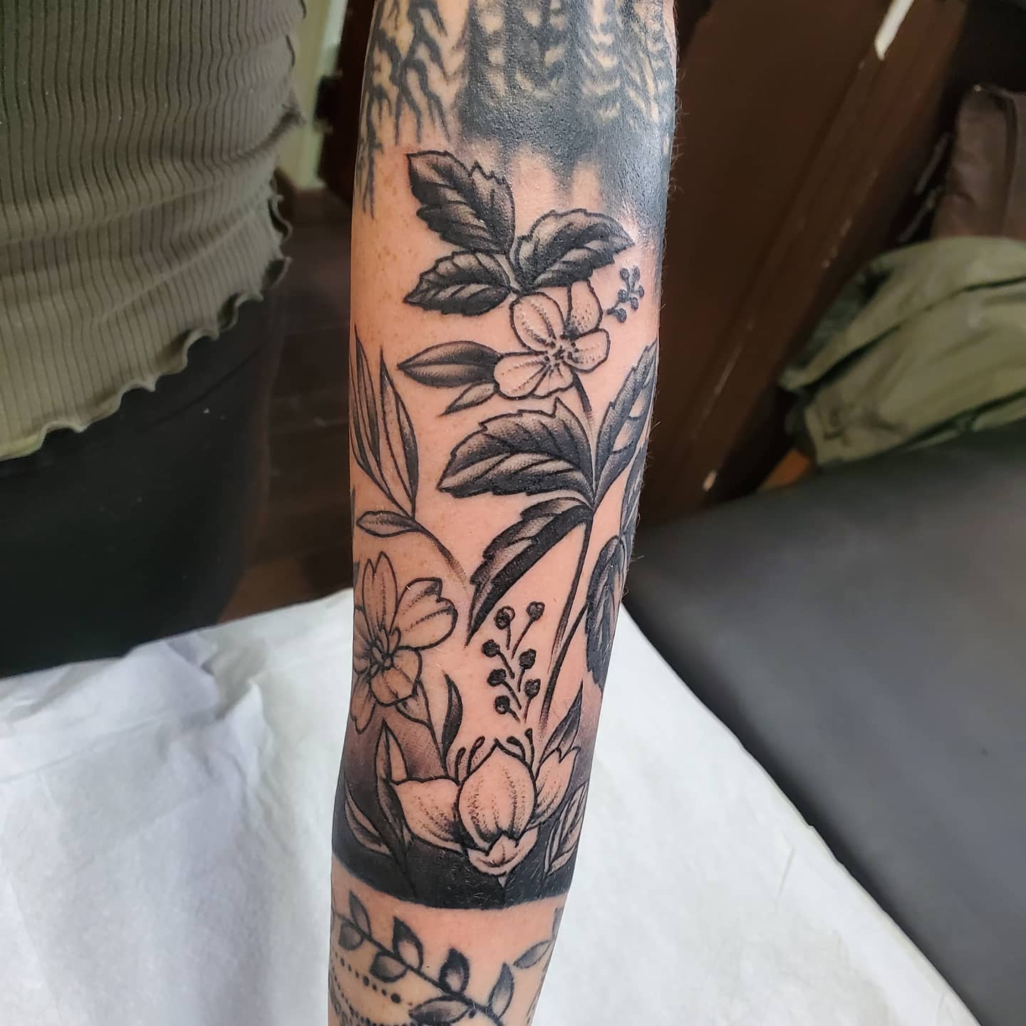 Black and gray floral tattoo sleeve on an arm featuring various flowers and leaves