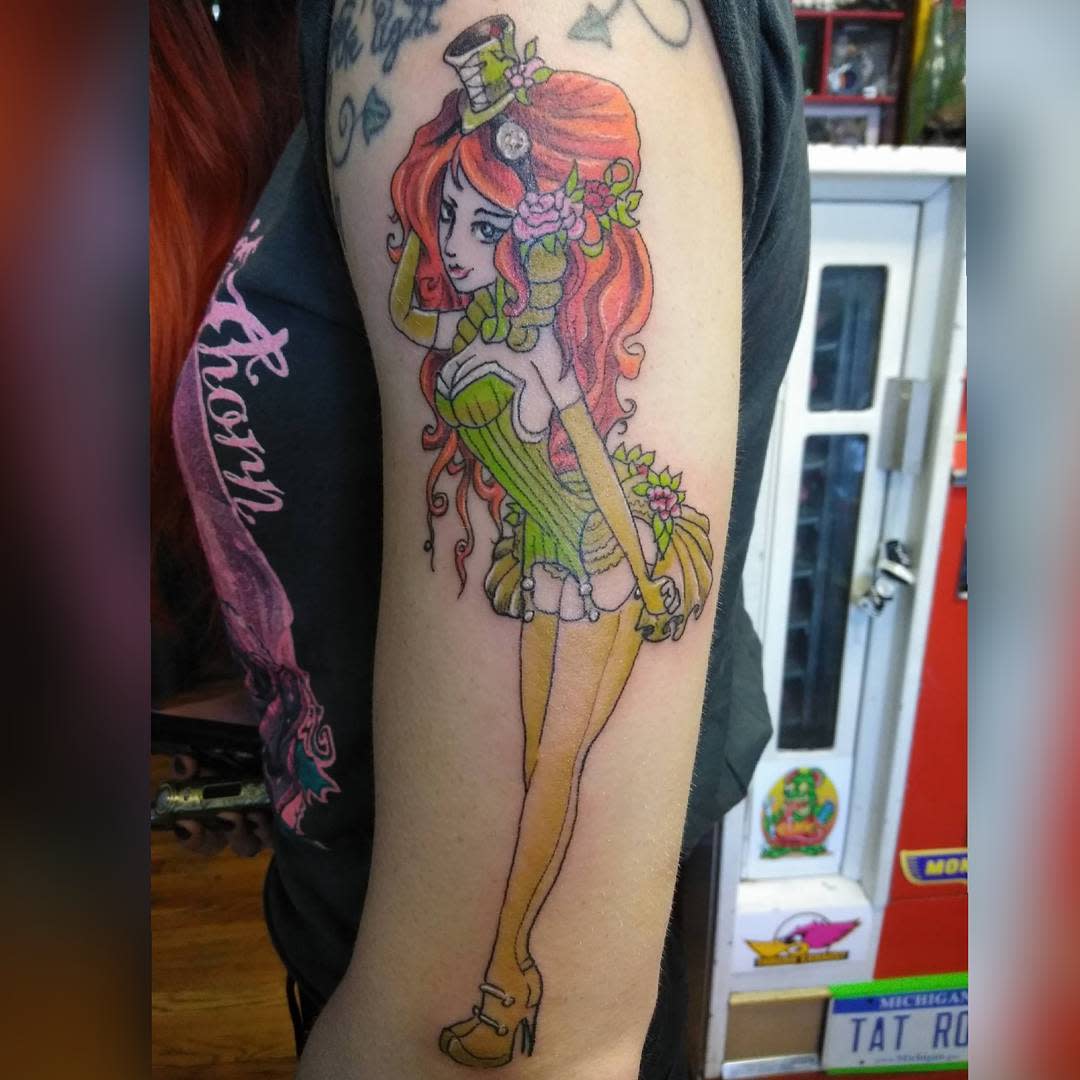 Colorful tattoo of a pin-up girl with red hair, wearing a green corset and top hat