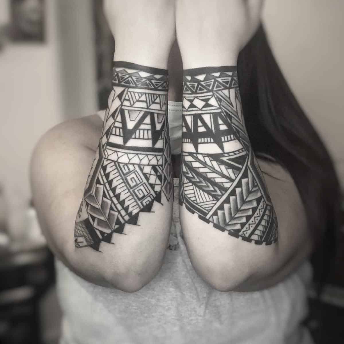 Forearm tattoos with intricate, geometric black ink designs extending from wrists featuring stunning Polynesian patterns