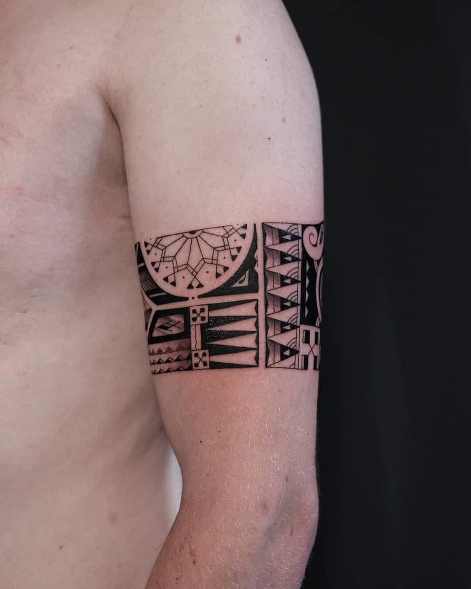 A tattooed upper arm with a black Polynesian tribal design against a dark background