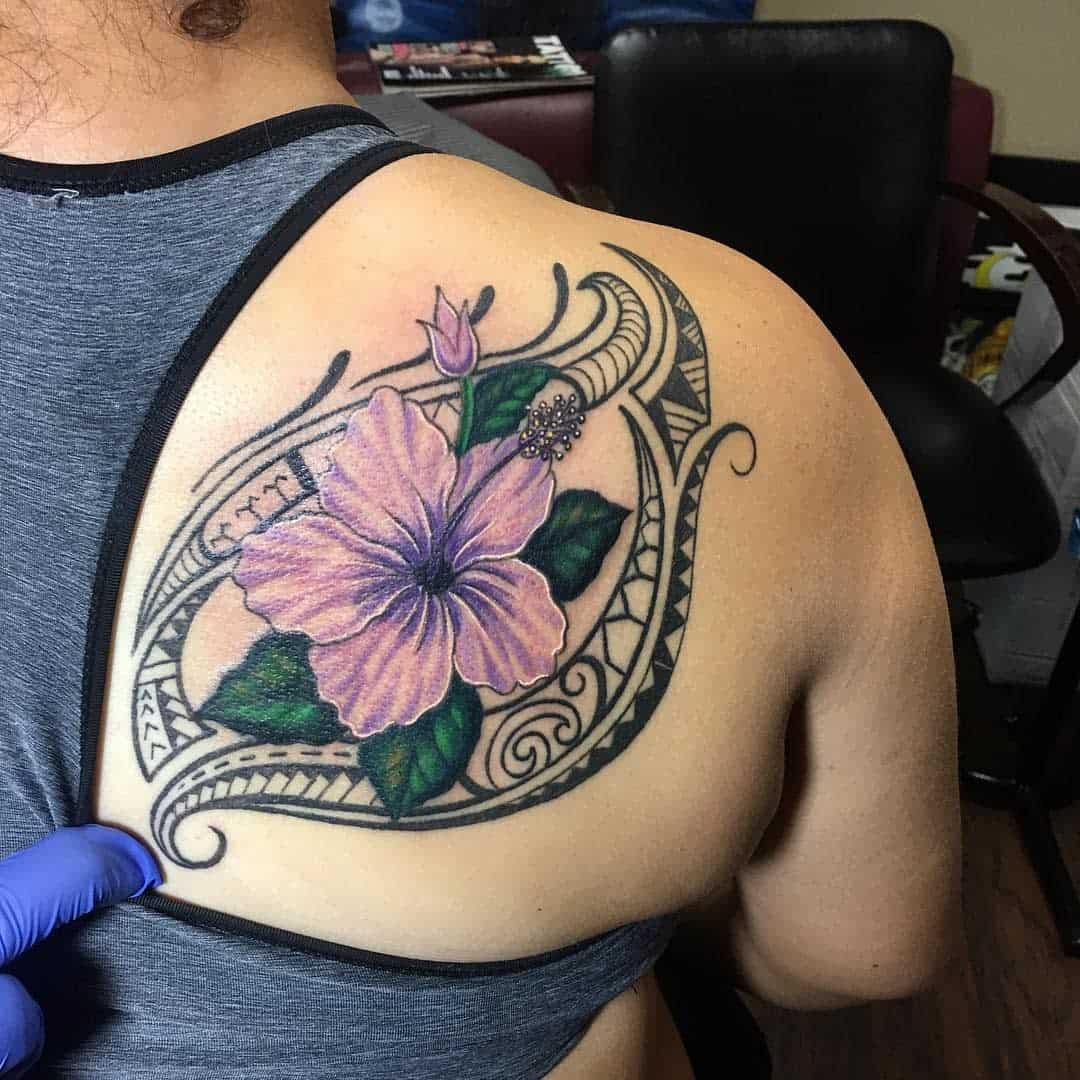 Close-up of a shoulder tattoo featuring a pink hibiscus flower intertwined with intricate black and Polynesian geometric designs